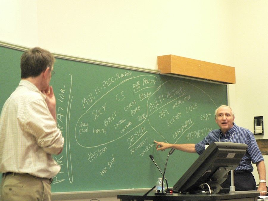 Ben Shneiderman pointing at a chalkboard with different design terms while talking to a man.