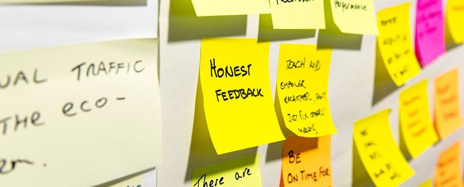 A selection of post-it notes stucks to a wall. The post-it note in focus says "honest feedback".