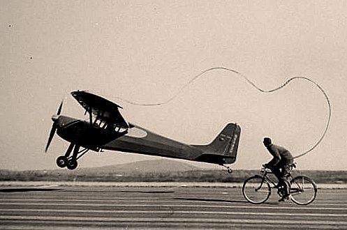 Picture of man riding a bycicle which is tied up to a plane by a cord.
