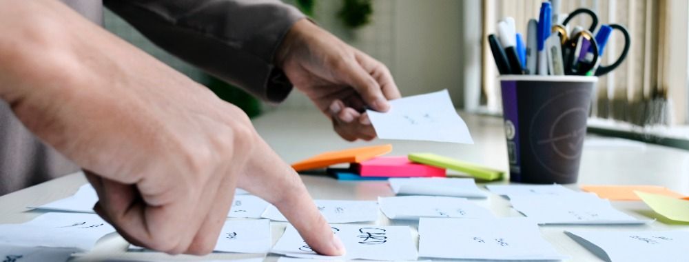 Photo of two hands working with sticky notes on a desk.