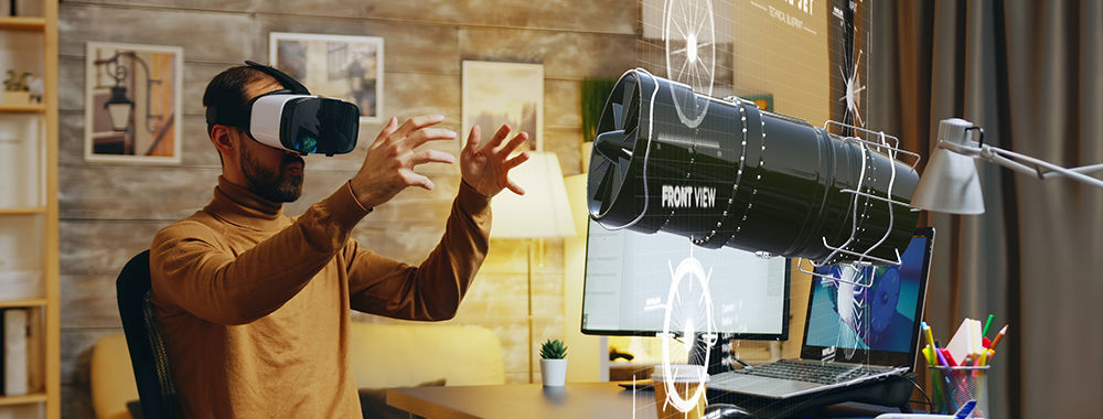 A man using a VR headset in front of a computer screen. In front of the computer screen is what looks like a virtual turbine or engine. The man is gesturing with his hands as if he's interacting with it.