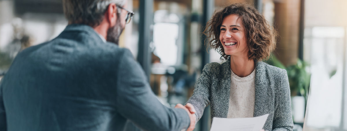 A confident woman smiling and shaking hands with a hiring manager during a successful job interview, illustrating how strong presentation skills lead to career success.