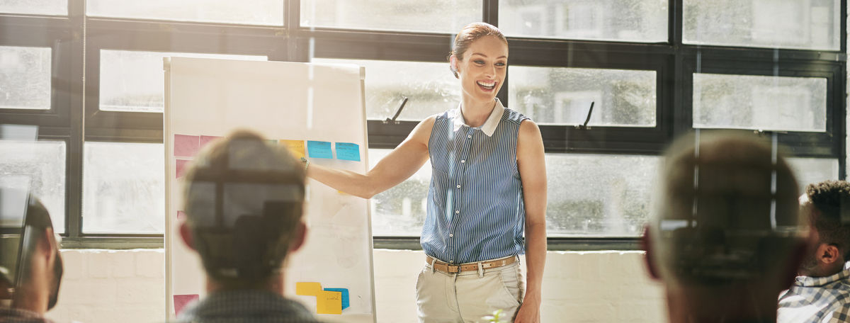 Confident woman presenting in front of a whiteboard, speaking clearly and gesturing with ease, conveying professionalism and expertise.