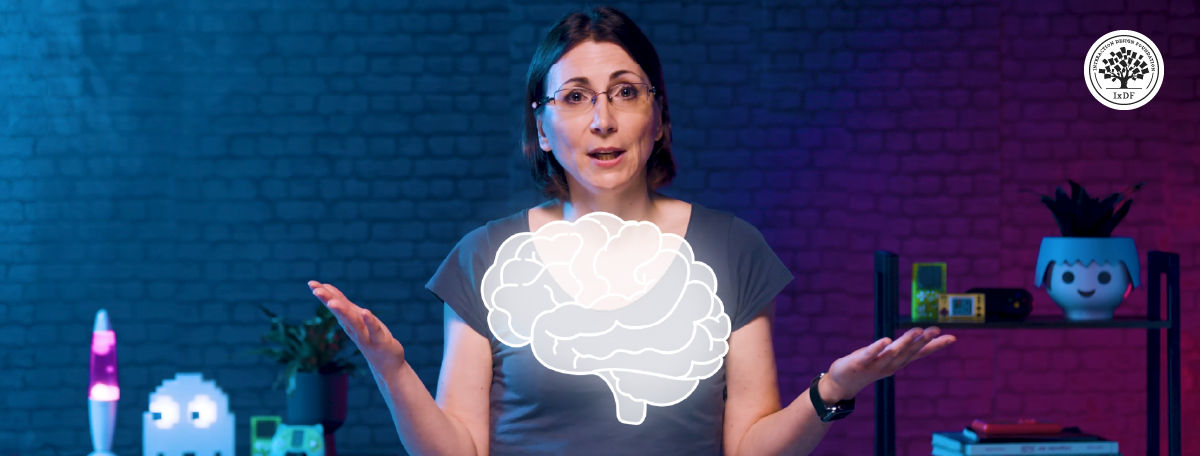 Game UX strategist Celia Hodent gestures with open hands against a neon-lit brick wall, with a white brain illustration overlaid on her chest.