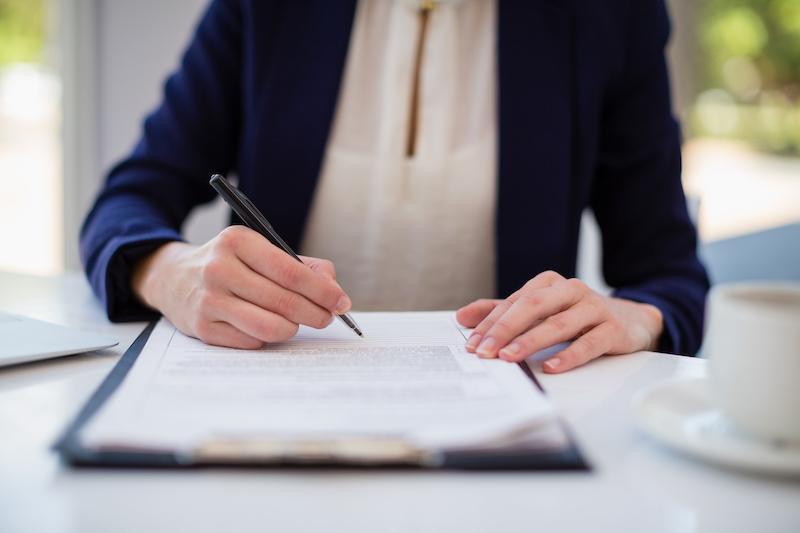 A woman writing on paper that's clipped to a board.