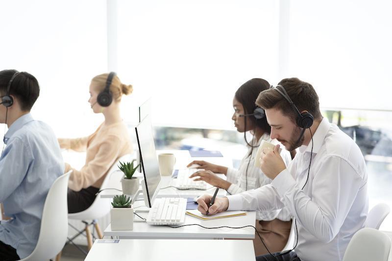 People in an office, talking to customers over the computer and taking notes simultaneously.