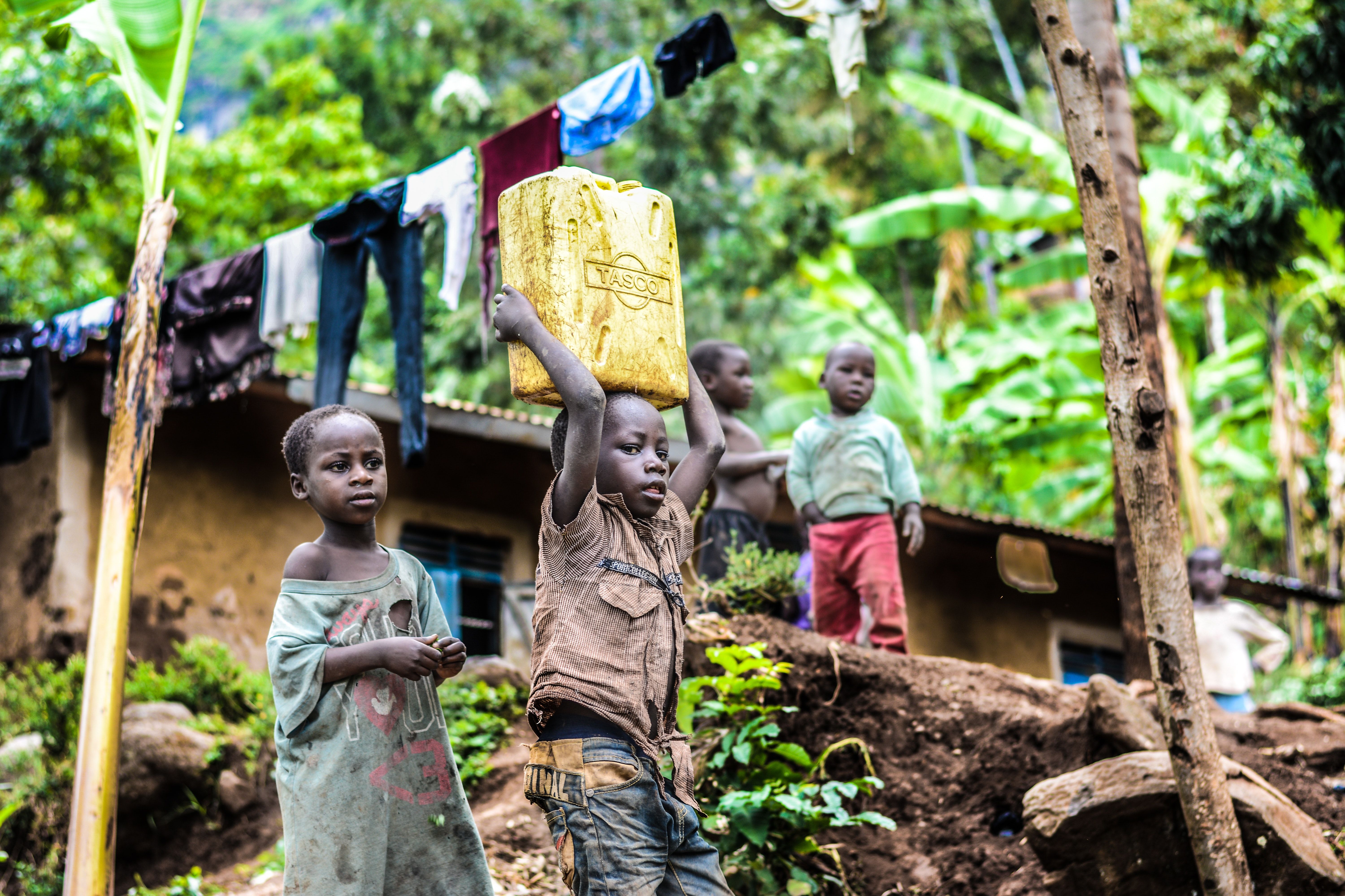 A child in Uganda carries a big box on his head, as other children look on.