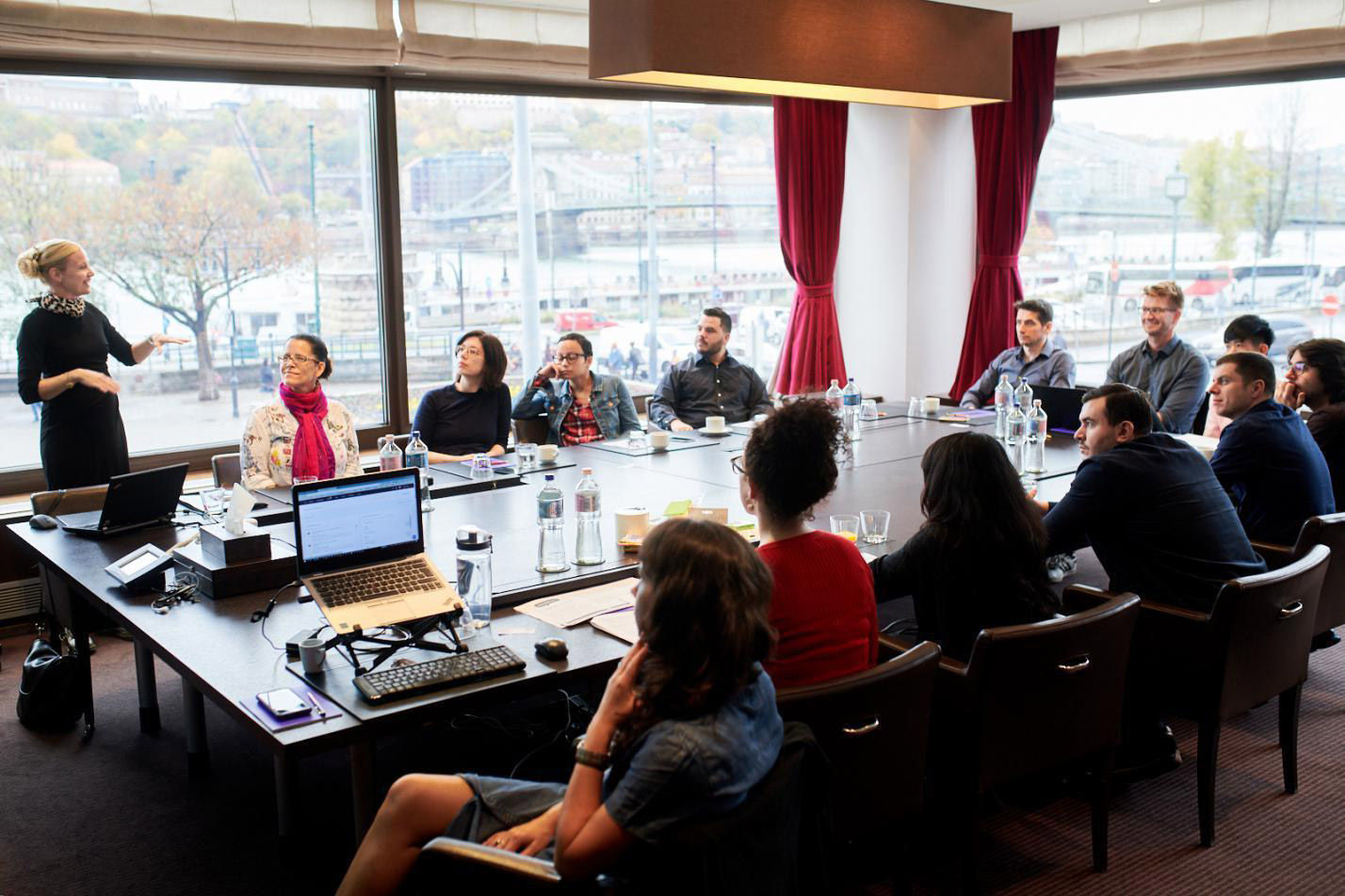 People seated around a large table, as one person gives a presentation.