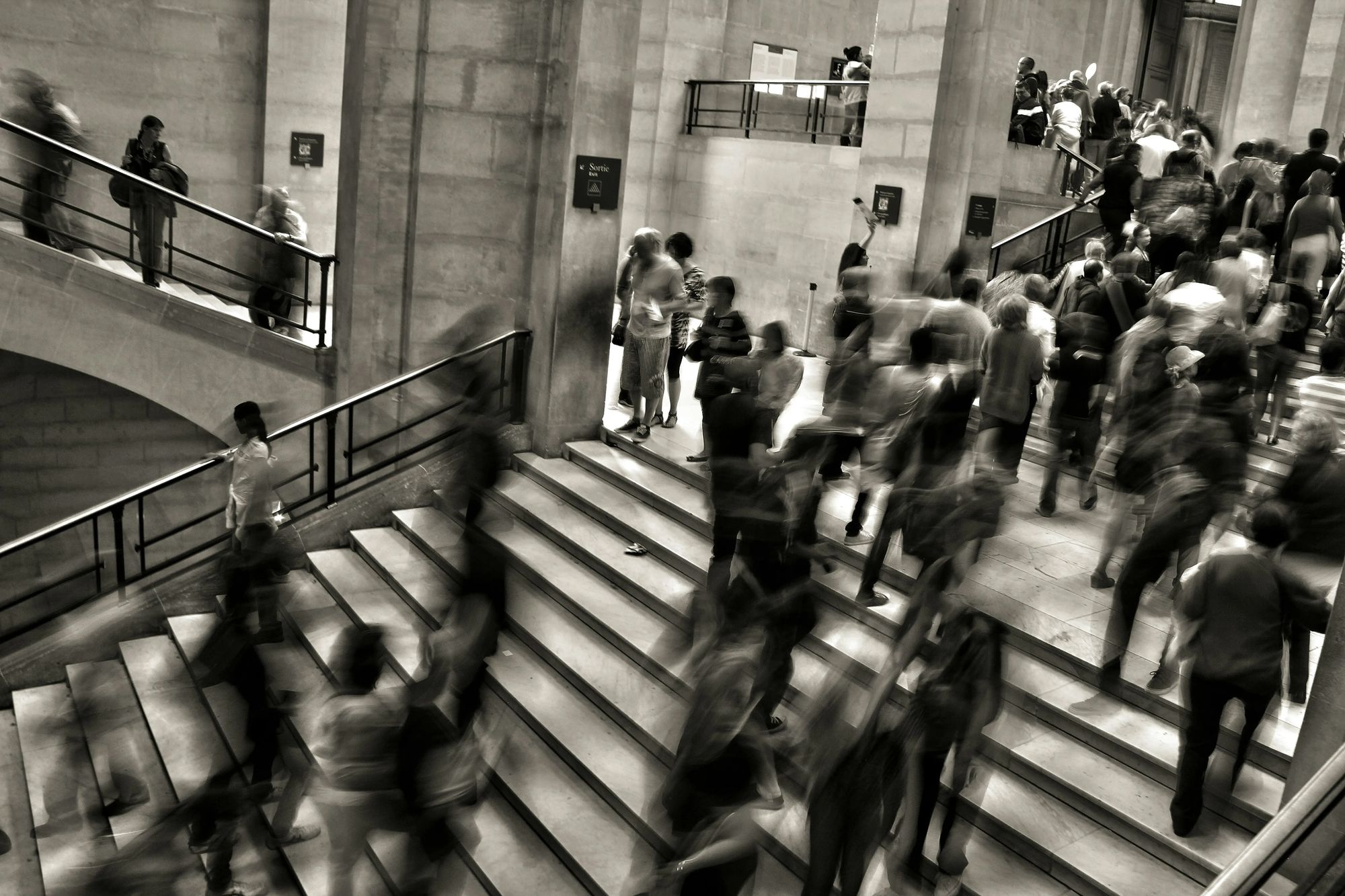 Black-and-white photo of a crowded indoor staircase with people moving in different directions, creating a blurred sense of motion and busyness. Overlaid text reads: “tech.fast. Crafting Calm In Chaos (Co-host IxDF). Featuring Nashmil Mobasseri, User Experience Designer at Softhouse.” A button says “GET YOUR SPOT!” and below it: “21 MAY 08:30–09:30 • SOFTHOUSE.
